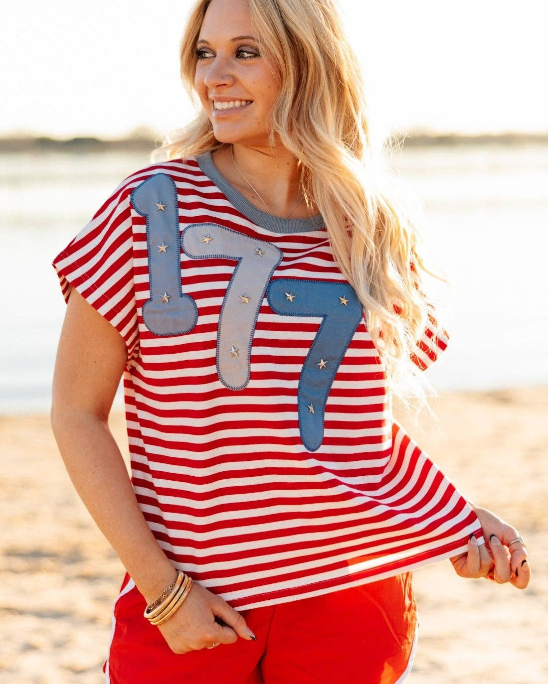 a high-stretch oversized short-sleeve stripe top with a crew neckline, a horizontal stripe pattern (red and white), bold denim 1776 patch detail, tiny star accents, a relaxed easy drape, and unlined