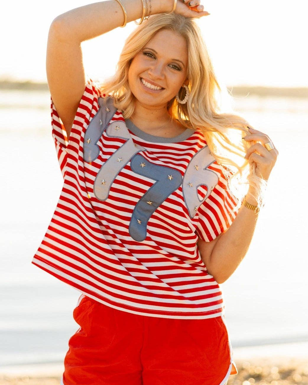 a high-stretch oversized short-sleeve stripe top with a crew neckline, a horizontal stripe pattern (red and white), bold denim 1776 patch detail, tiny star accents, a relaxed easy drape, and unlined
