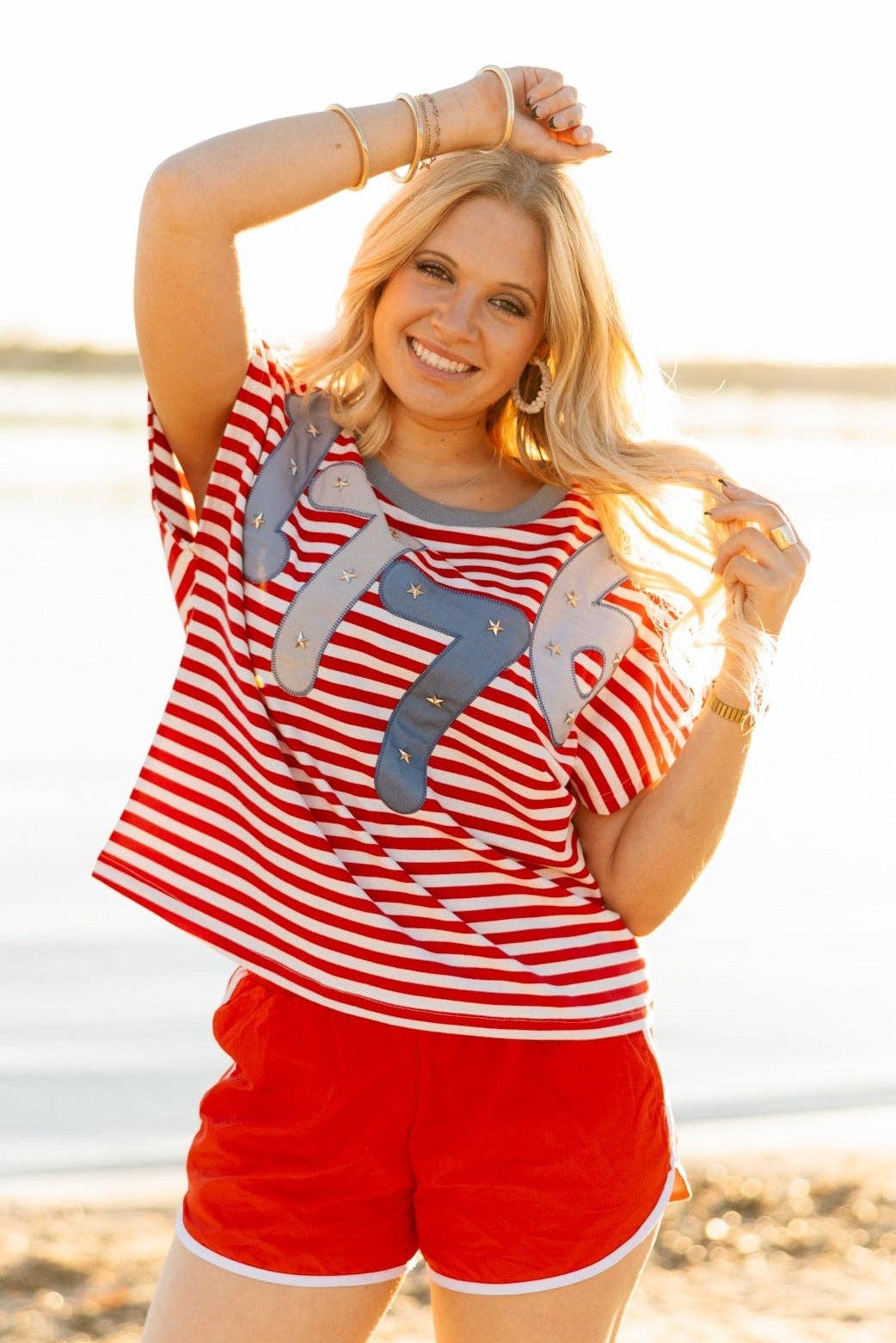 a high-stretch oversized short-sleeve stripe top with a crew neckline, a horizontal stripe pattern (red and white), bold denim 1776 patch detail, tiny star accents, a relaxed easy drape, and unlined