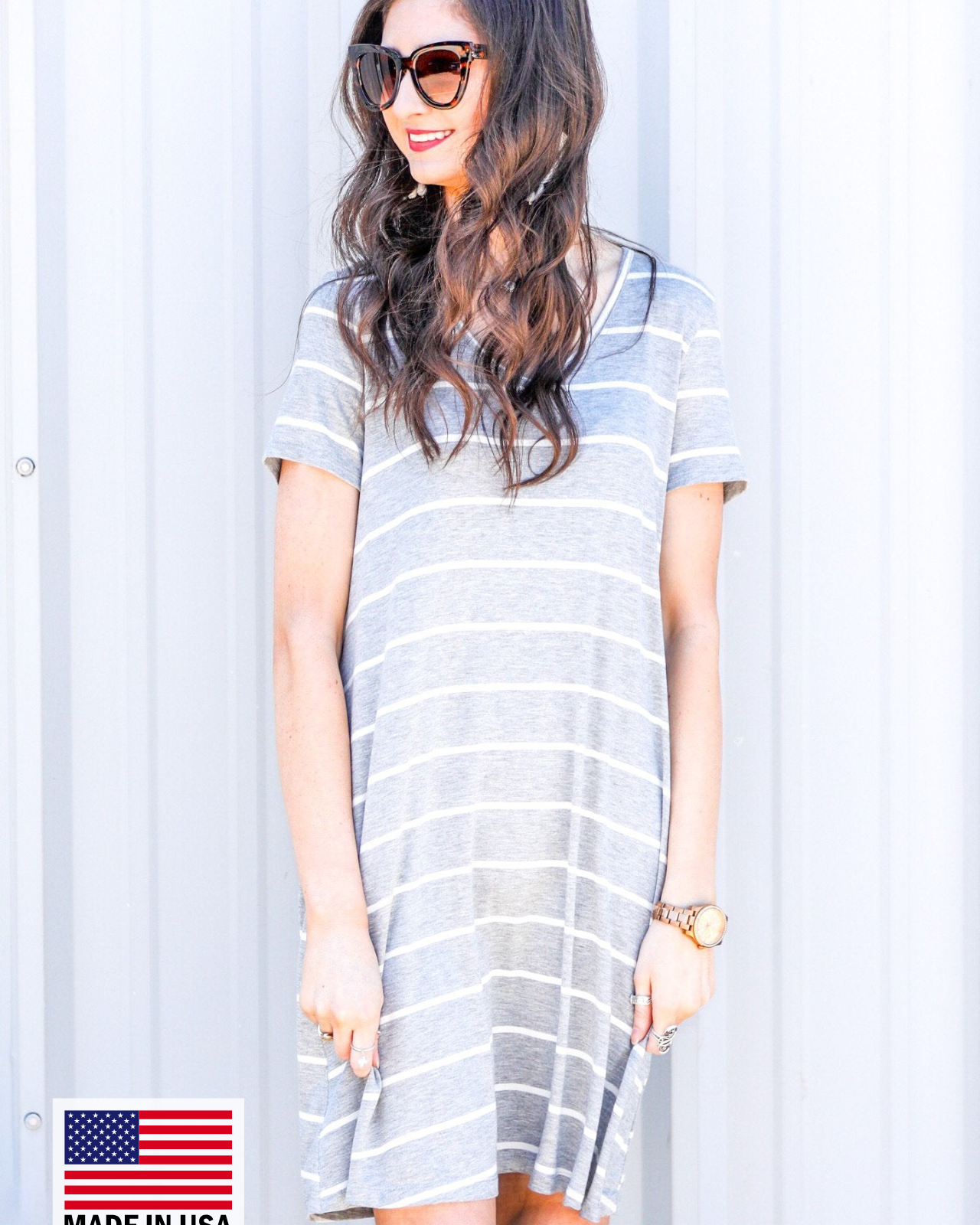 a soft stretchy knit dress with a V-neckline, short sleeves, a relaxed A-line silhouette, a straight hemline, and a horizontal white stripe pattern on a solid heathered grey background with a MADE IN USA watermark in the bottom left hand corner