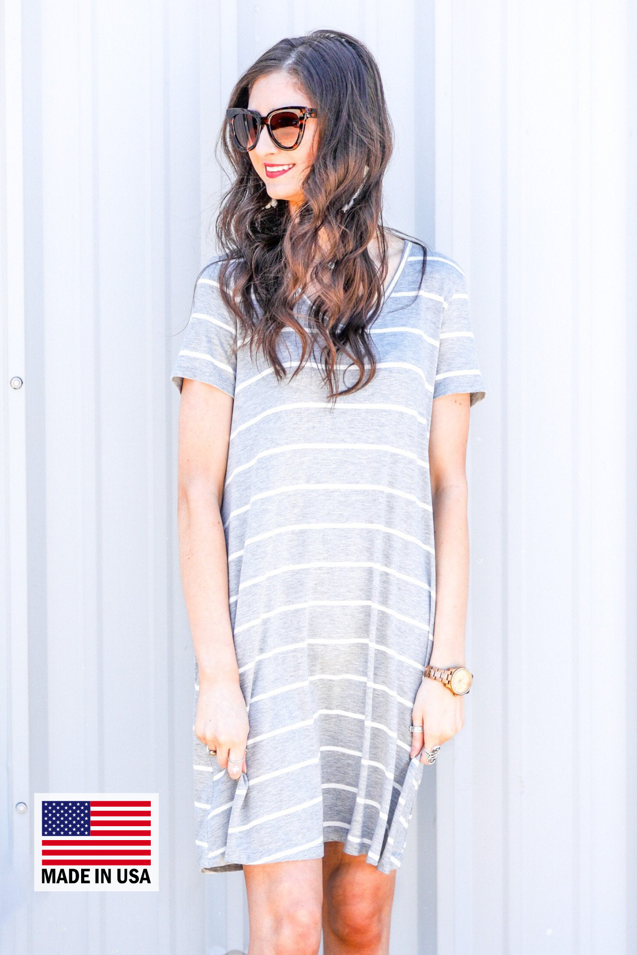 a soft stretchy knit dress with a V-neckline, short sleeves, a relaxed A-line silhouette, a straight hemline, and a horizontal white stripe pattern on a solid heathered grey background with a MADE IN USA watermark in the bottom left hand corner