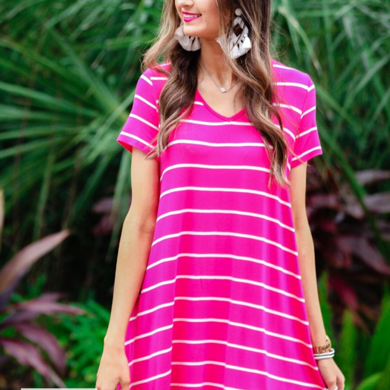 a soft stretchy knit dress with a V-neckline, short sleeves, a relaxed A-line silhouette, a straight hemline, and a horizontal white stripe pattern on a solid hot pink background with a MADE IN USA watermark in the bottom left hand corner