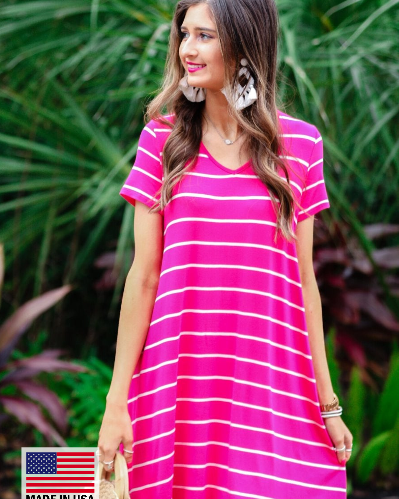 a soft stretchy knit dress with a V-neckline, short sleeves, a relaxed A-line silhouette, a straight hemline, and a horizontal white stripe pattern on a solid hot pink background with a MADE IN USA watermark in the bottom left hand corner