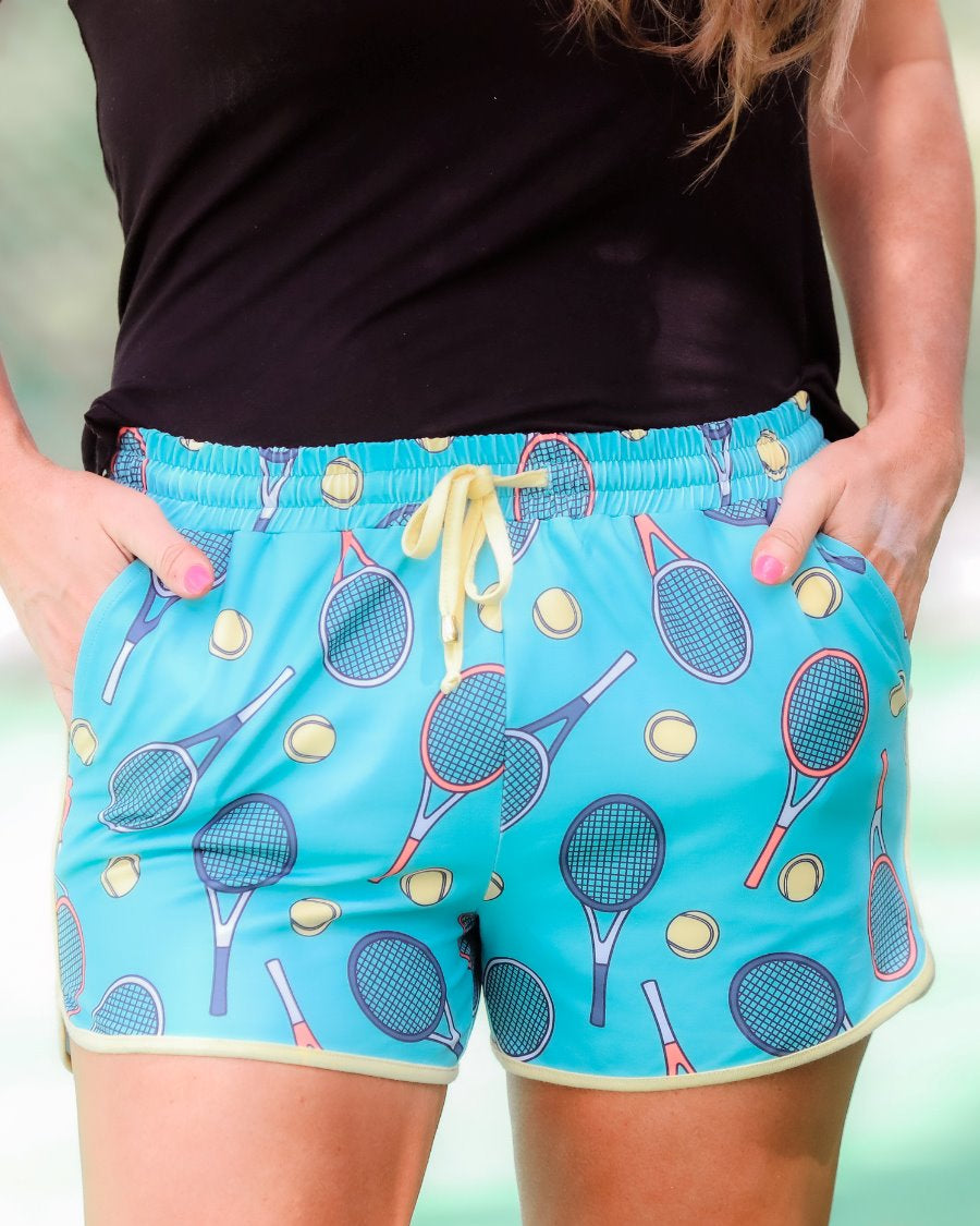 mid-rise relaxed fit activewear shorts with side pockets and a tie waist drawstring with gold bead accents, designed on a tennis pattern print fabric, cadet blue base, and yellow trim