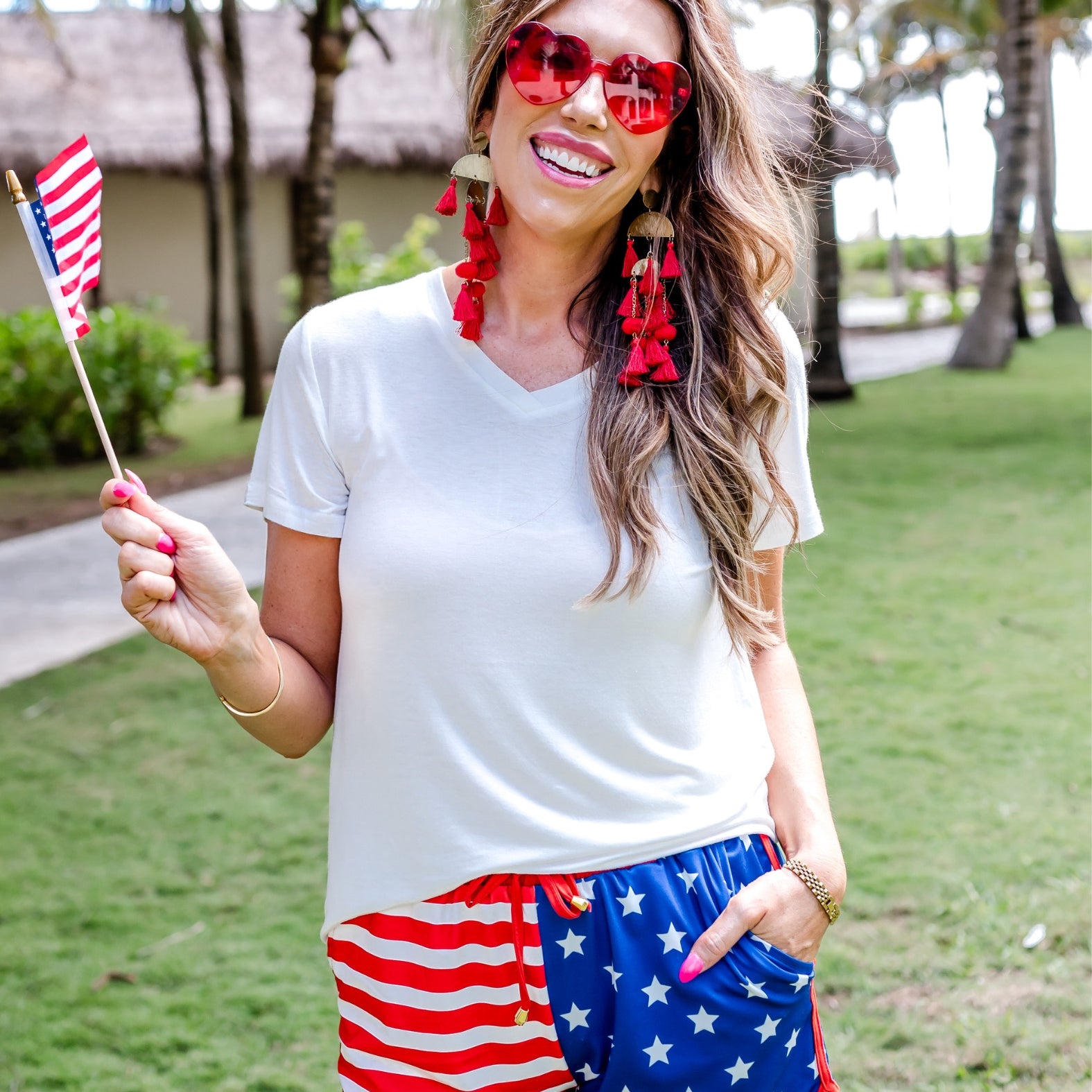 mid-rise relaxed fit activewear shorts with side pockets and a tie waist drawstring with gold bead accents, designed on a mix of stars (blue and white) and stripes (red and white) pattern print fabric and red trim