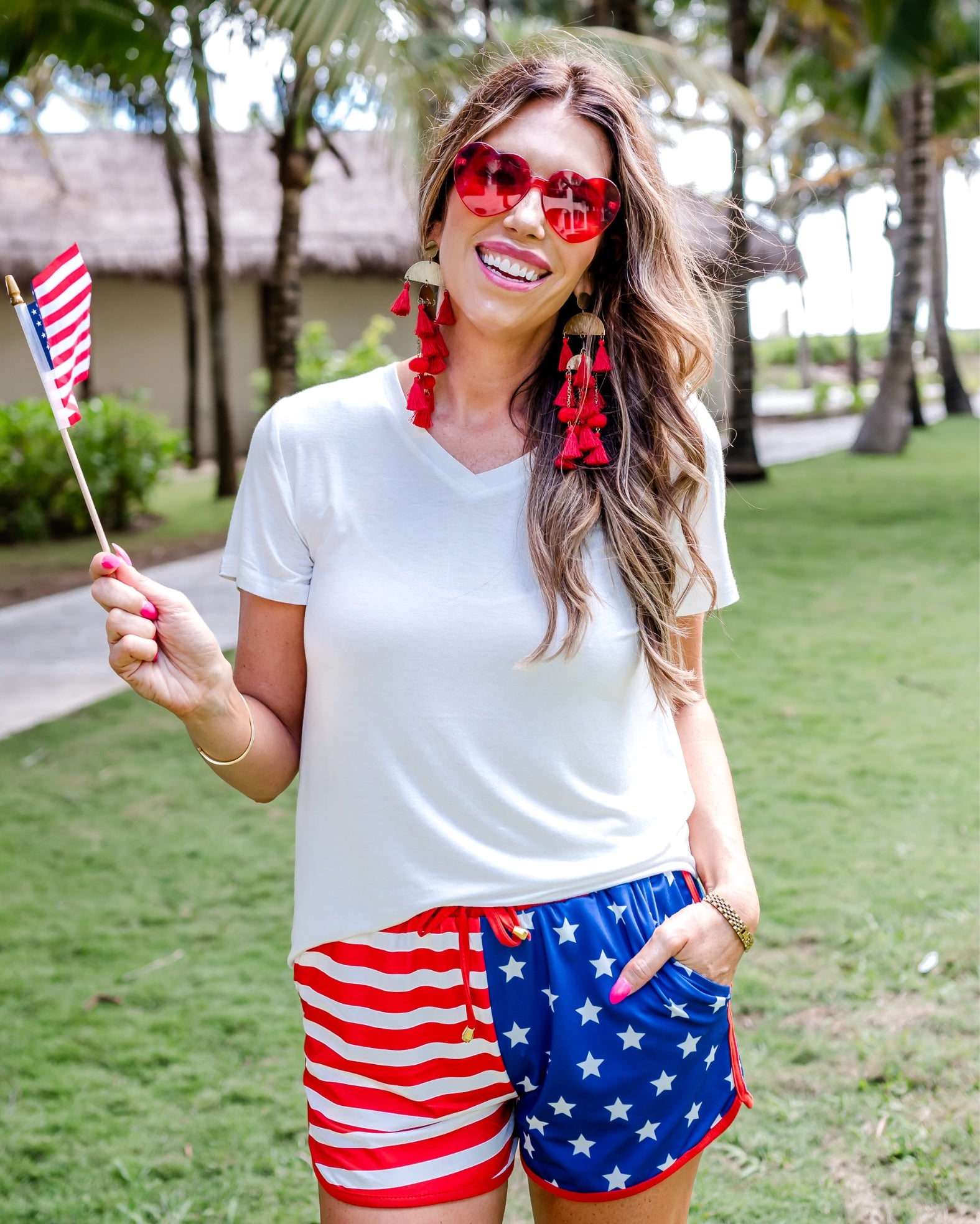 mid-rise relaxed fit activewear shorts with side pockets and a tie waist drawstring with gold bead accents, designed on a mix of stars (blue and white) and stripes (red and white) pattern print fabric and red trim