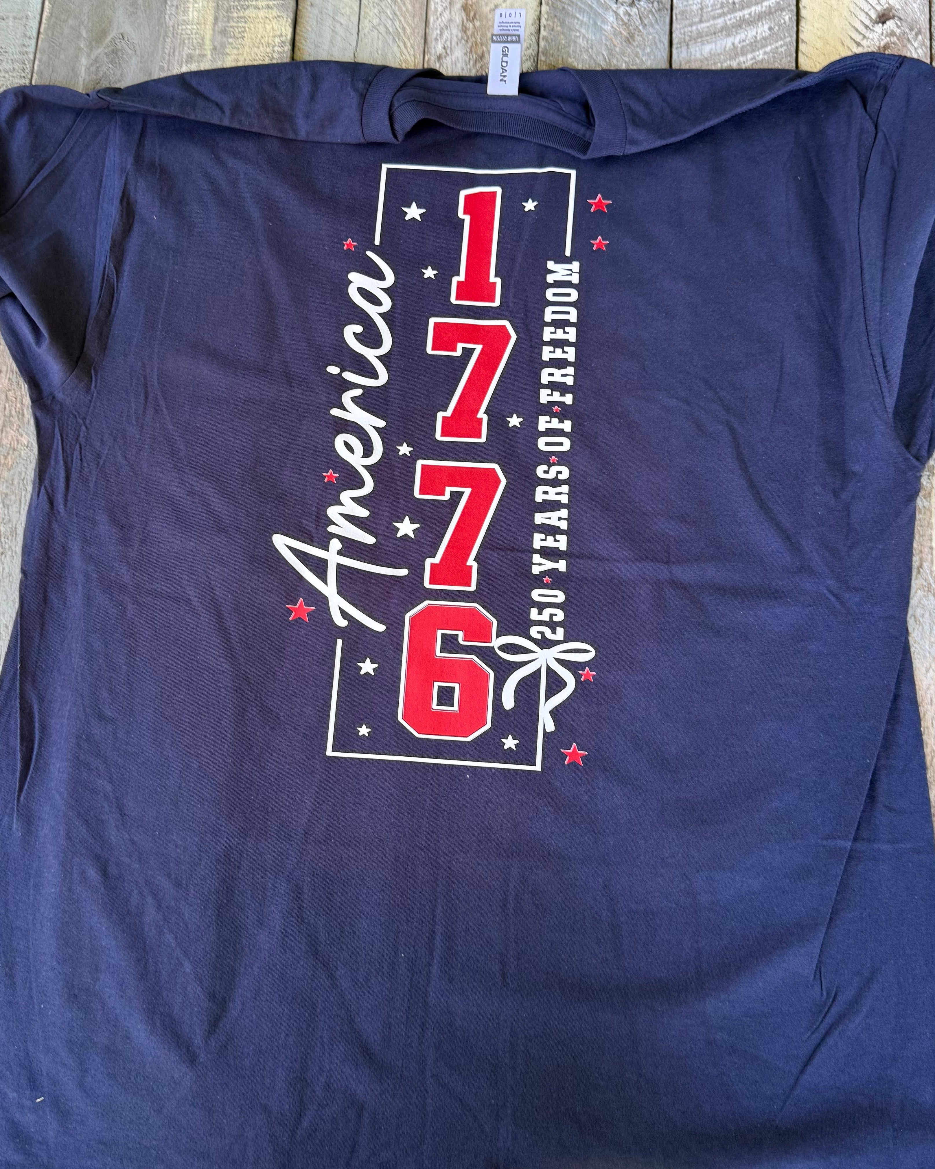 a soft navy unisex Gildan t-shirt with a crew neckline, short sleeves, a front America 250 chest graphic, a bold 1776 America back design, a 250 Years of Freedom detail, and an easy year-round fit