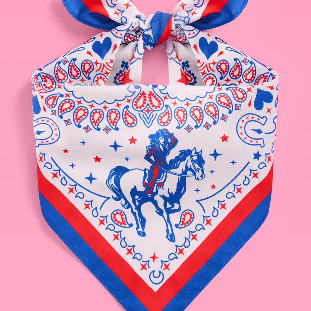 a square bandana with a red, white, and blue western-inspired print, complete with a bold border, cowgirls, hearts, horses, horseshoes, paisley accents, and stars