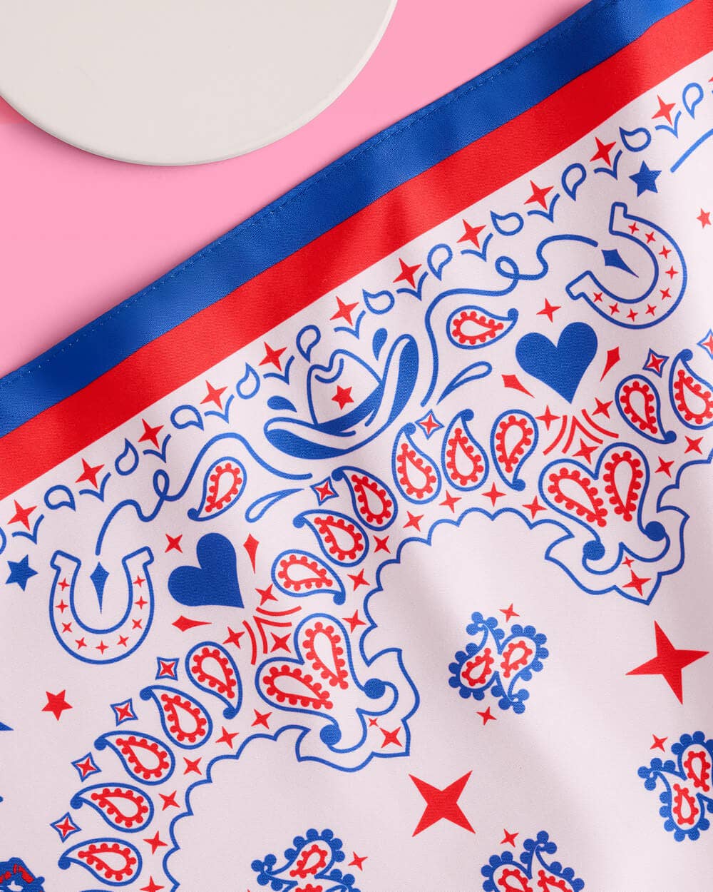 a square bandana with a red, white, and blue western-inspired print, complete with a bold border, cowgirls, hearts, horses, horseshoes, paisley accents, and stars