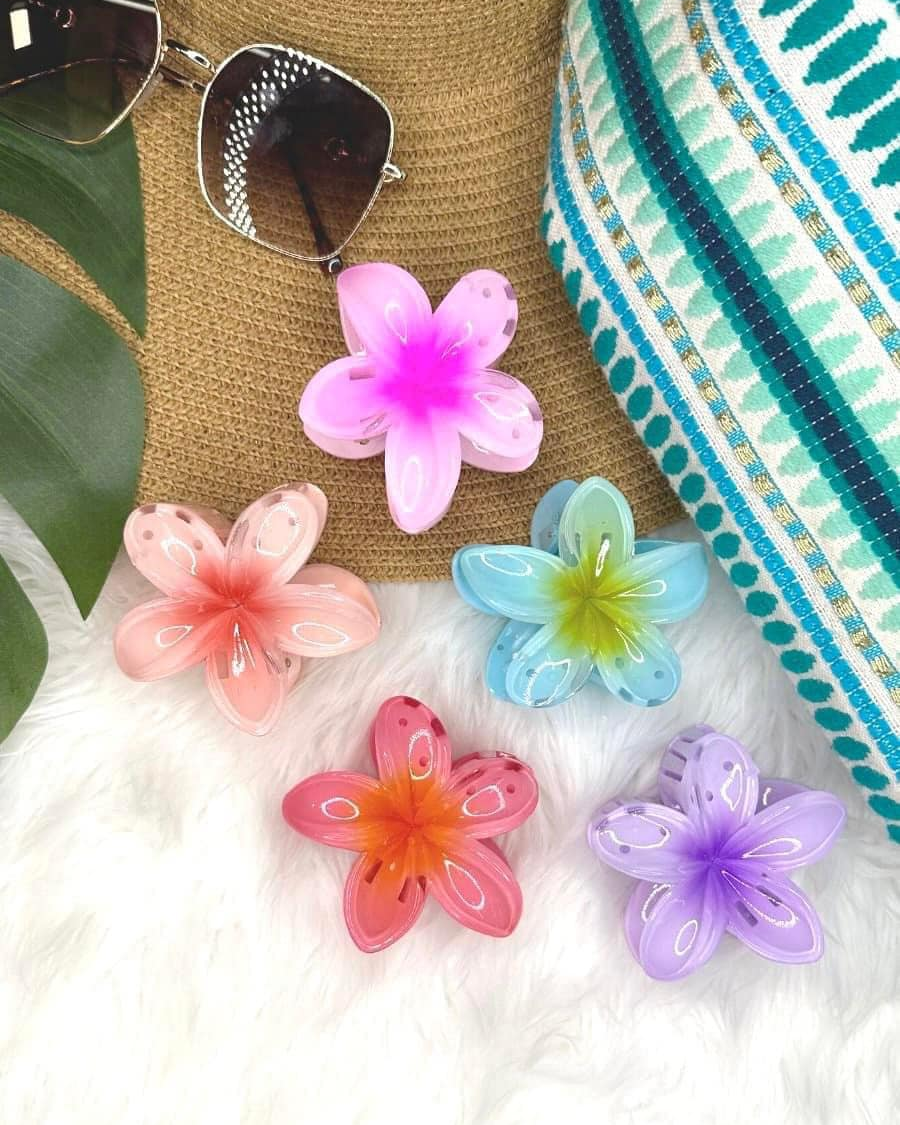 Colorful flower-shaped hair clips on a textured surface with sunglasses and a hat.