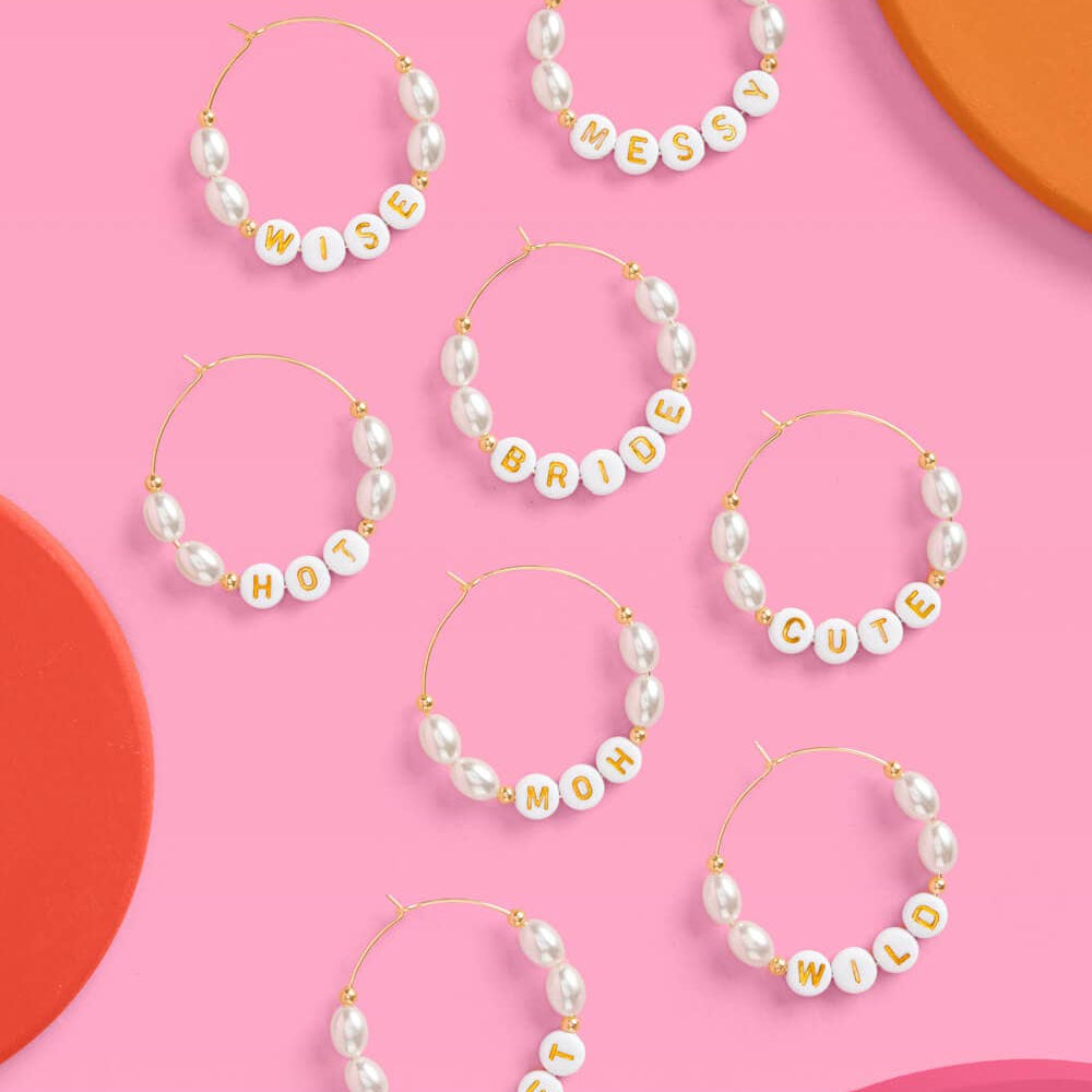 Set of pearl hoop earrings with personalized name charms on a pink background