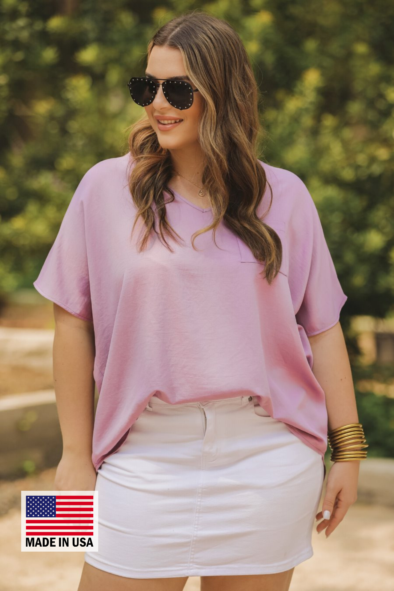 a lightweight lilac short-sleeve woven tunic with a V-neckline, a front chest pocket, and a relaxed, non-stretch silhouette, accented with a MADE IN USA watermark in the bottom left-hand corner