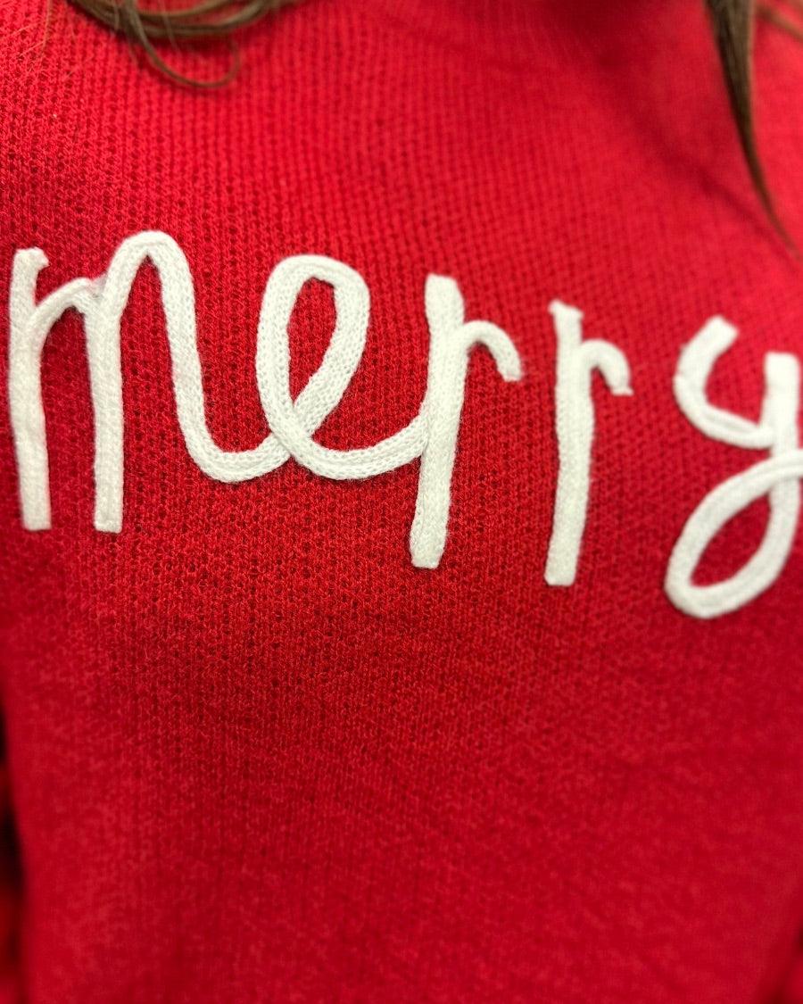 a red long-sleeve patterned sweater adorned with 'merry' script across the chest in white and ribbed detailing at the cuffs, neckline, and hem