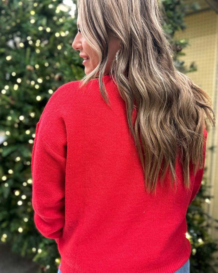 a red long-sleeve patterned sweater adorned with 'merry' script across the chest in white and ribbed detailing at the cuffs, neckline, and hem