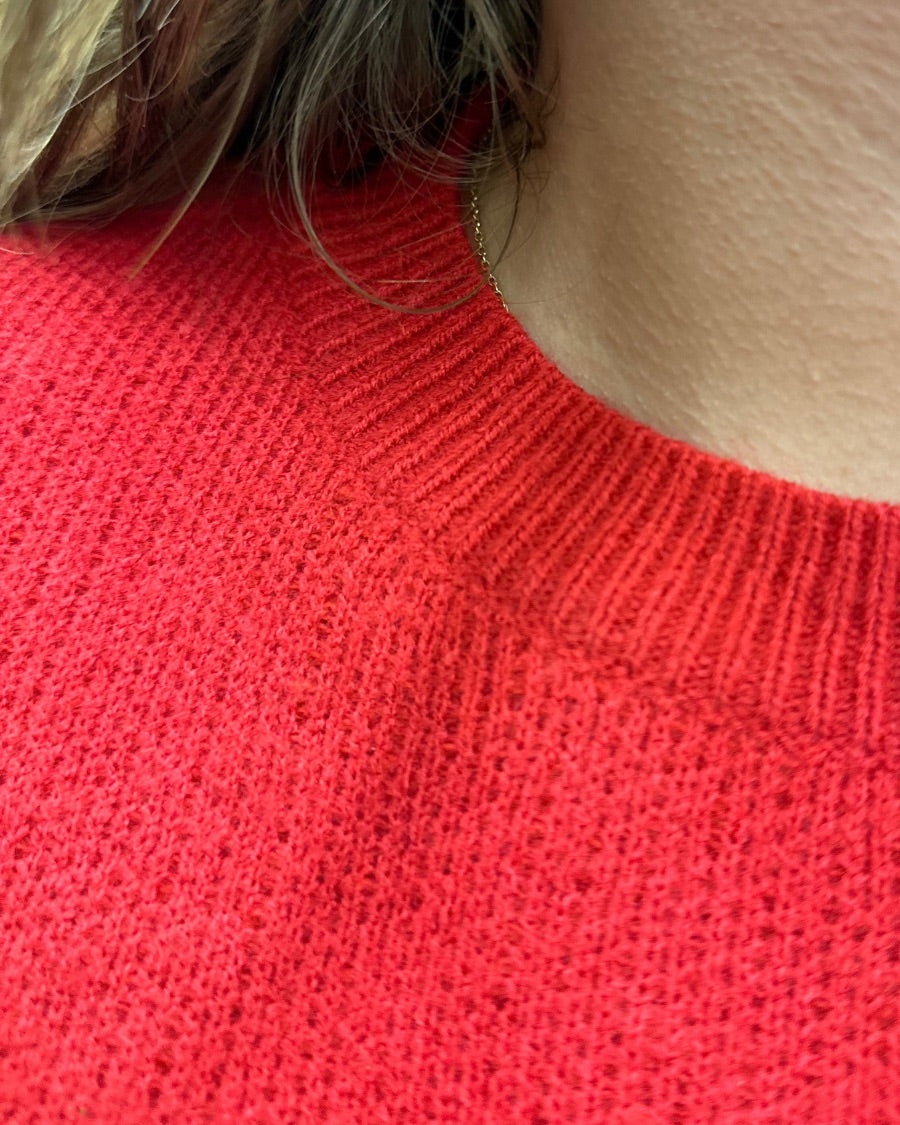 a red long-sleeve patterned sweater adorned with 'merry' script across the chest in white and ribbed detailing at the cuffs, neckline, and hem