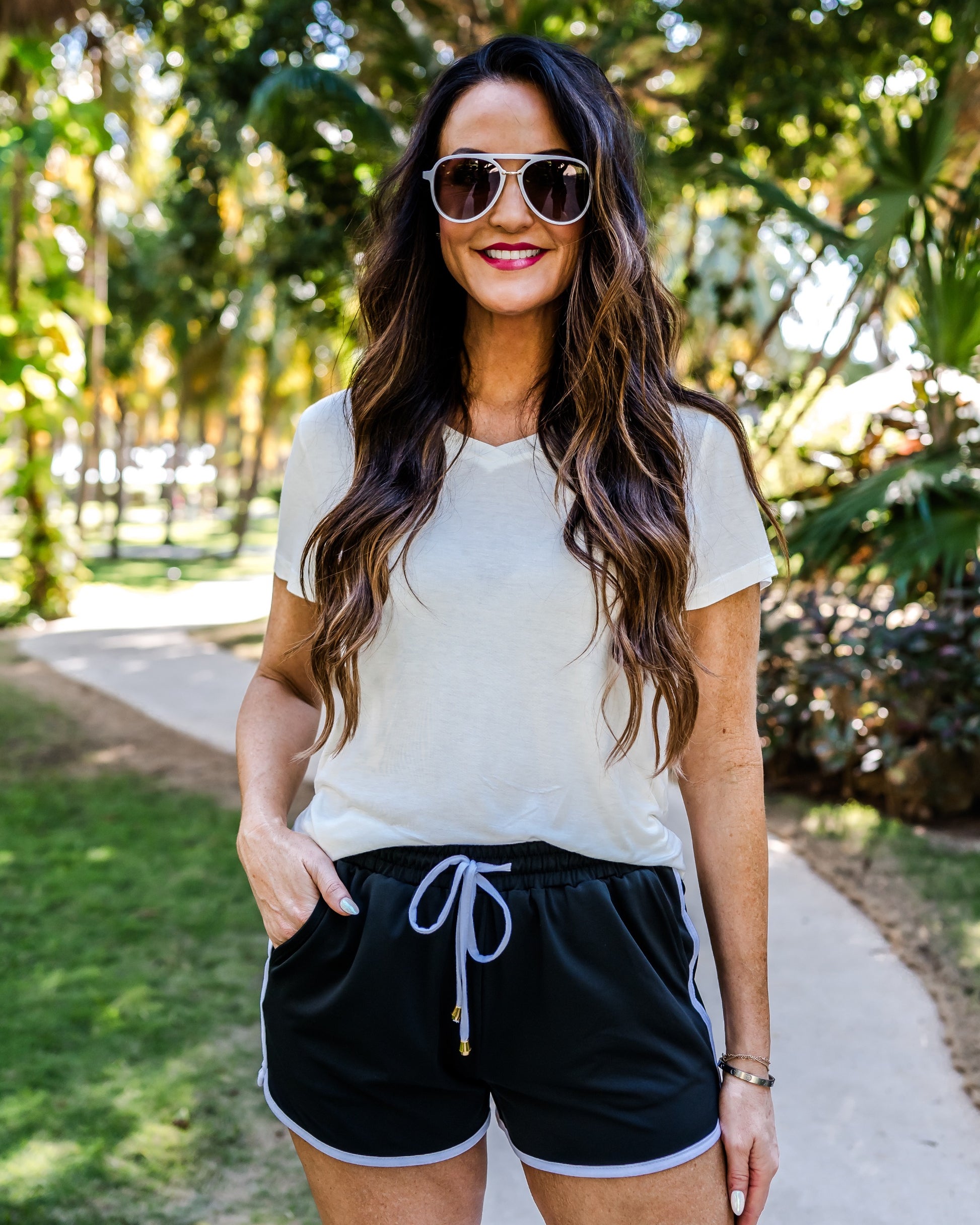 mid-rise relaxed fit activewear shorts with side pockets and a tie waist drawstring with gold bead accents, designed on a solid black print fabric and white trim