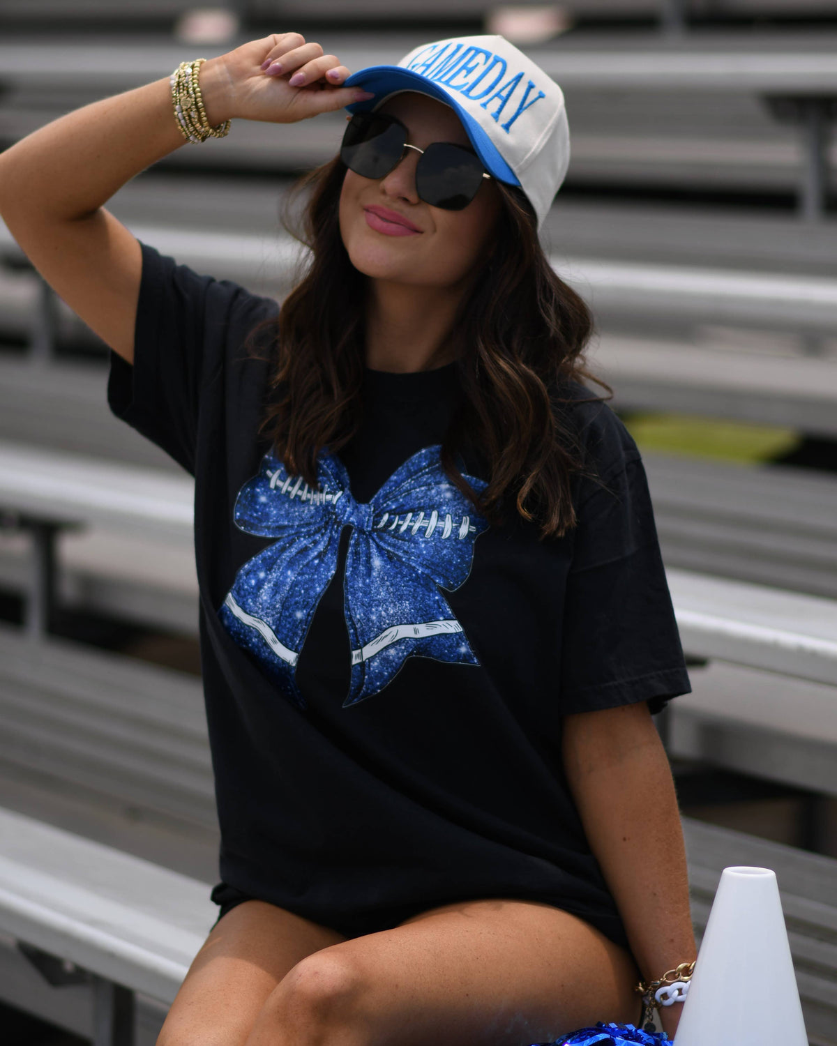 a black Comfort Colors tee crafted on soft garment-dyed cotton with a DTF-printed blue faux glitter football bow graphic, crew neckline, and short sleeves in both youth and adult sizing