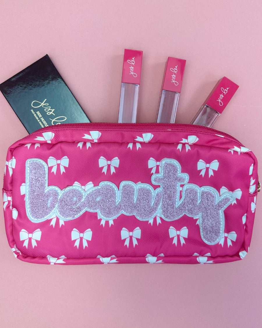 white bow pattern on a neon pink background travel bag with a zipper closure and a chenille patch bearing BEAUTY