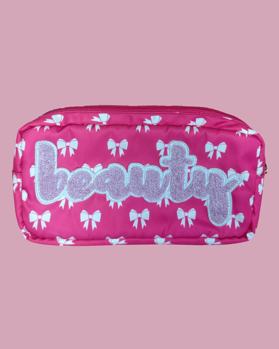 white bow pattern on a neon pink background travel bag with a zipper closure and a chenille patch bearing BEAUTY