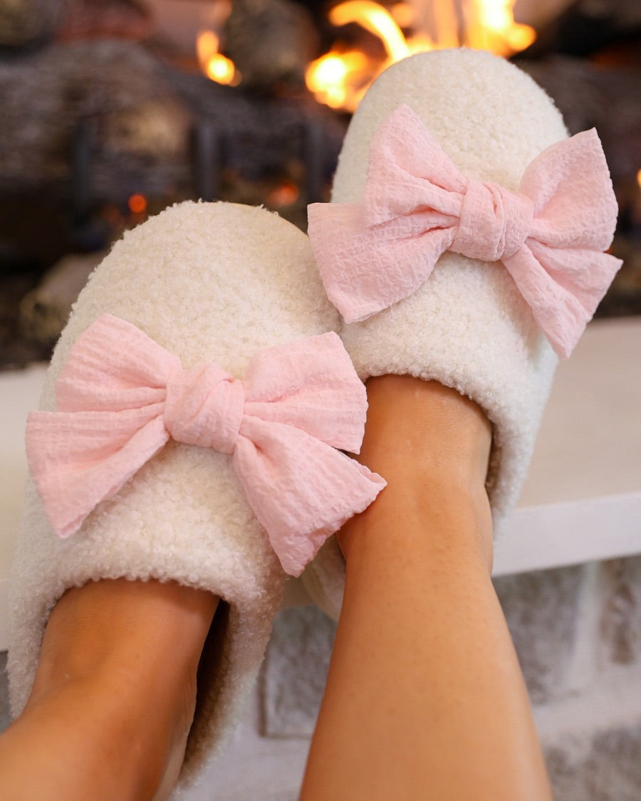 soft white plush slippers with a cozy cushioned sole and an oversized pink bow detail