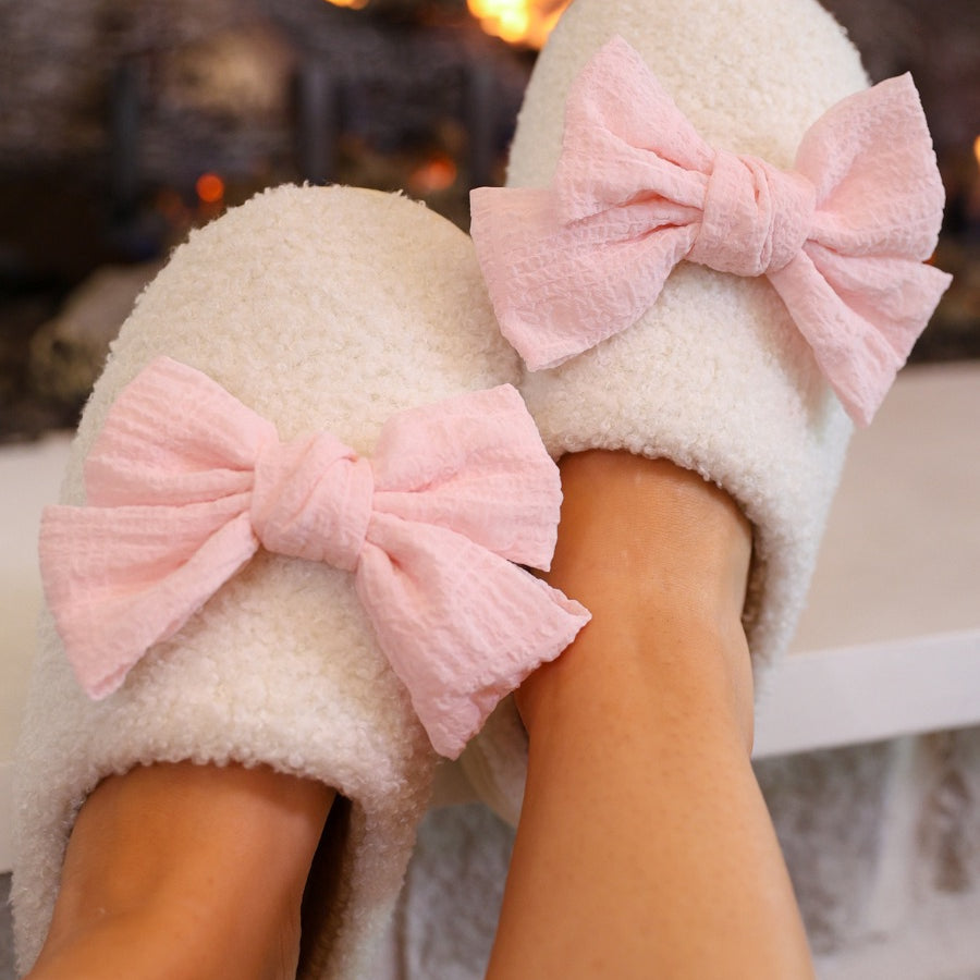 soft white plush slippers with a cozy cushioned sole and an oversized pink bow detail
