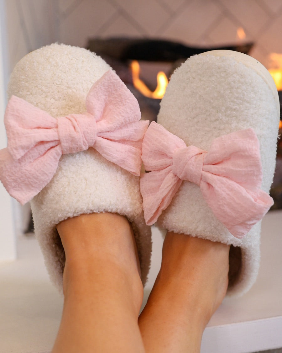 soft white plush slippers with a cozy cushioned sole and an oversized pink bow detail