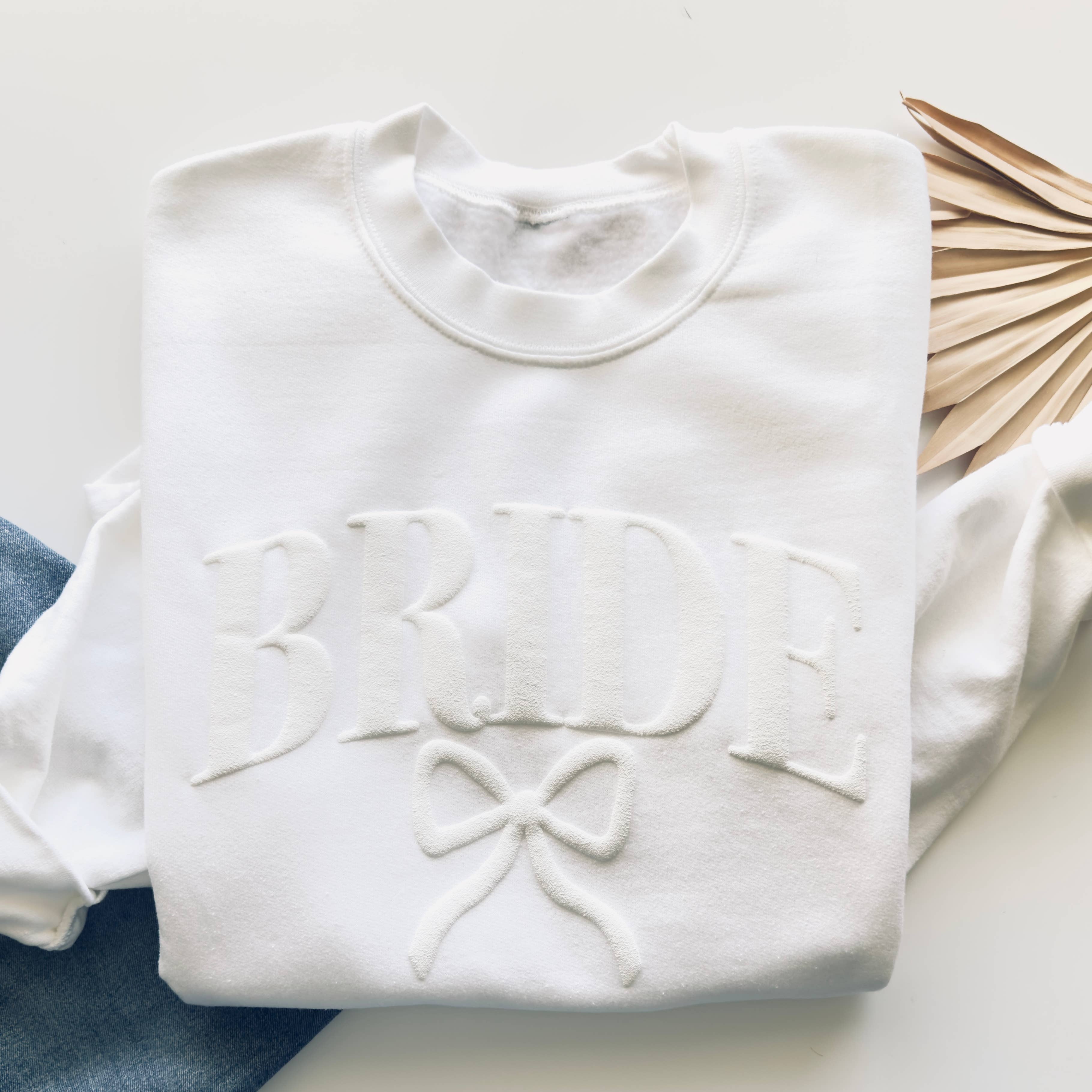 White sweatshirt with 'Bride' and bow design on a white surface