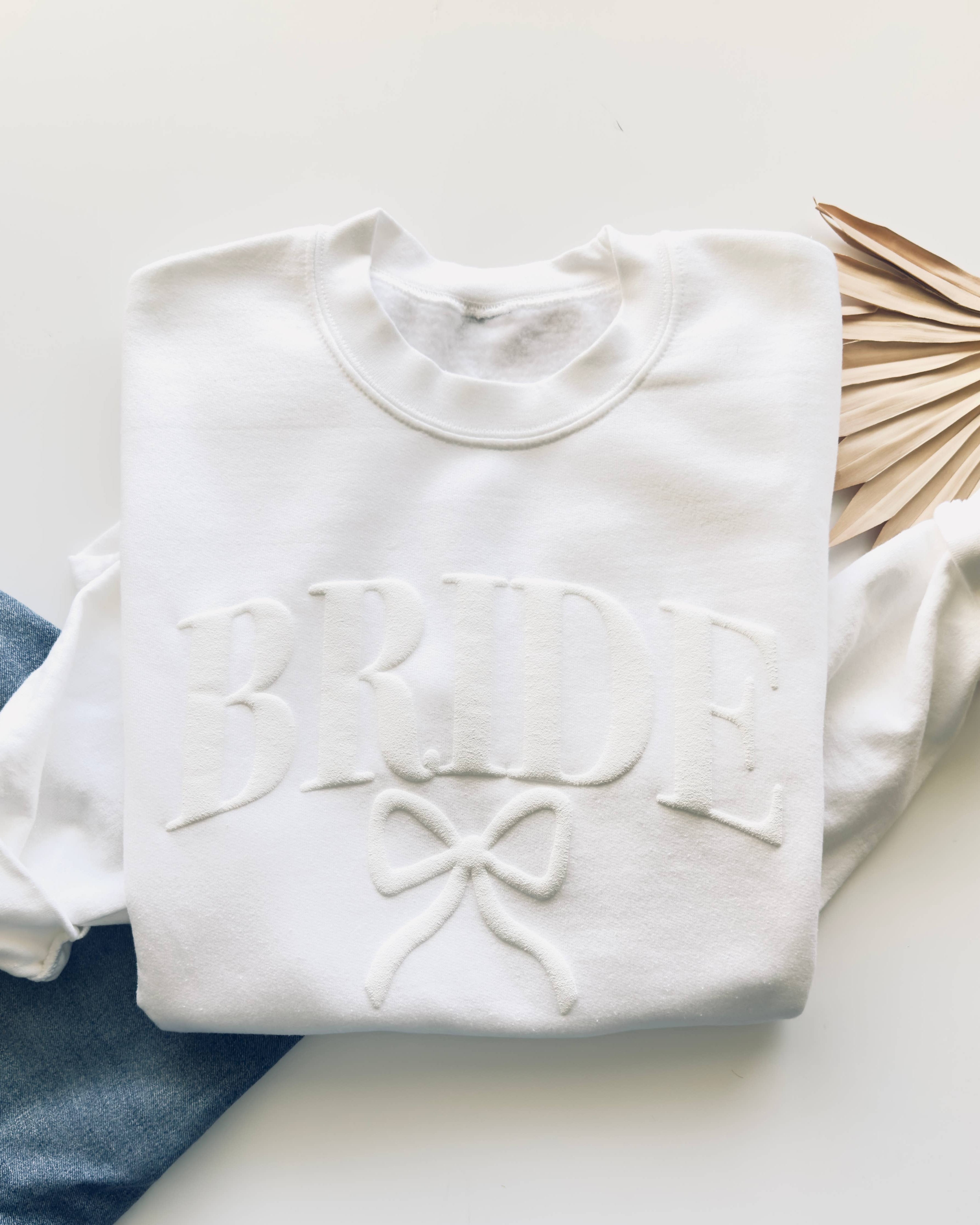White sweatshirt with 'Bride' and bow design on a white surface