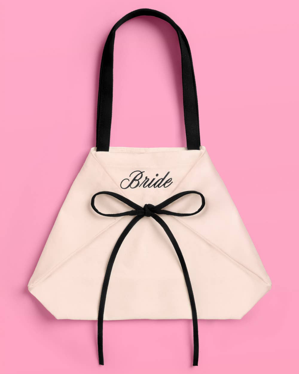 a roomy canvas tote with black embroidered 'Bride' script, black shoulder straps, and bow tie detail