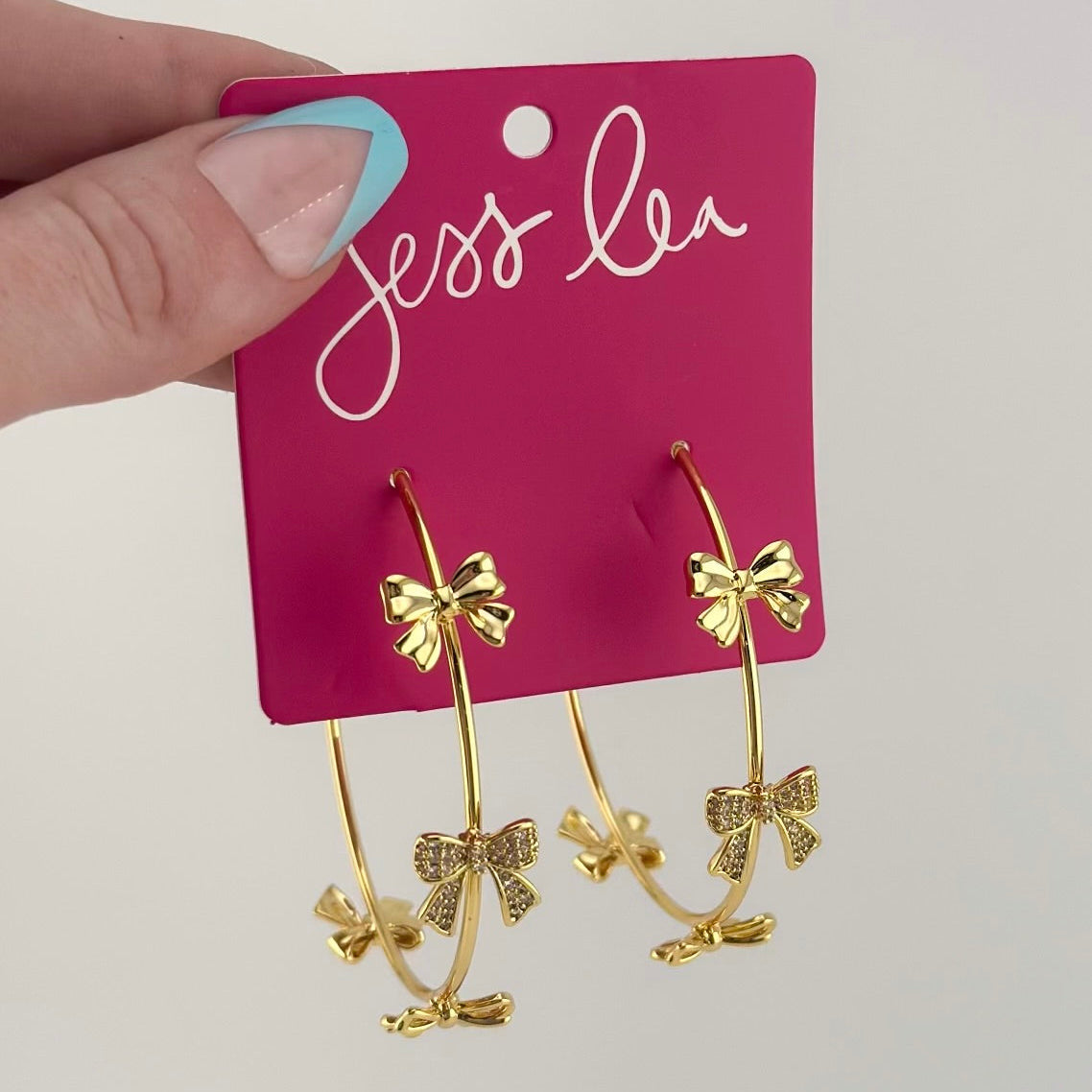 gold hoop earring with a post back and a comfort earring back in gold adorned in two solid bows, one open bow, and one bow adorned in rhinestones