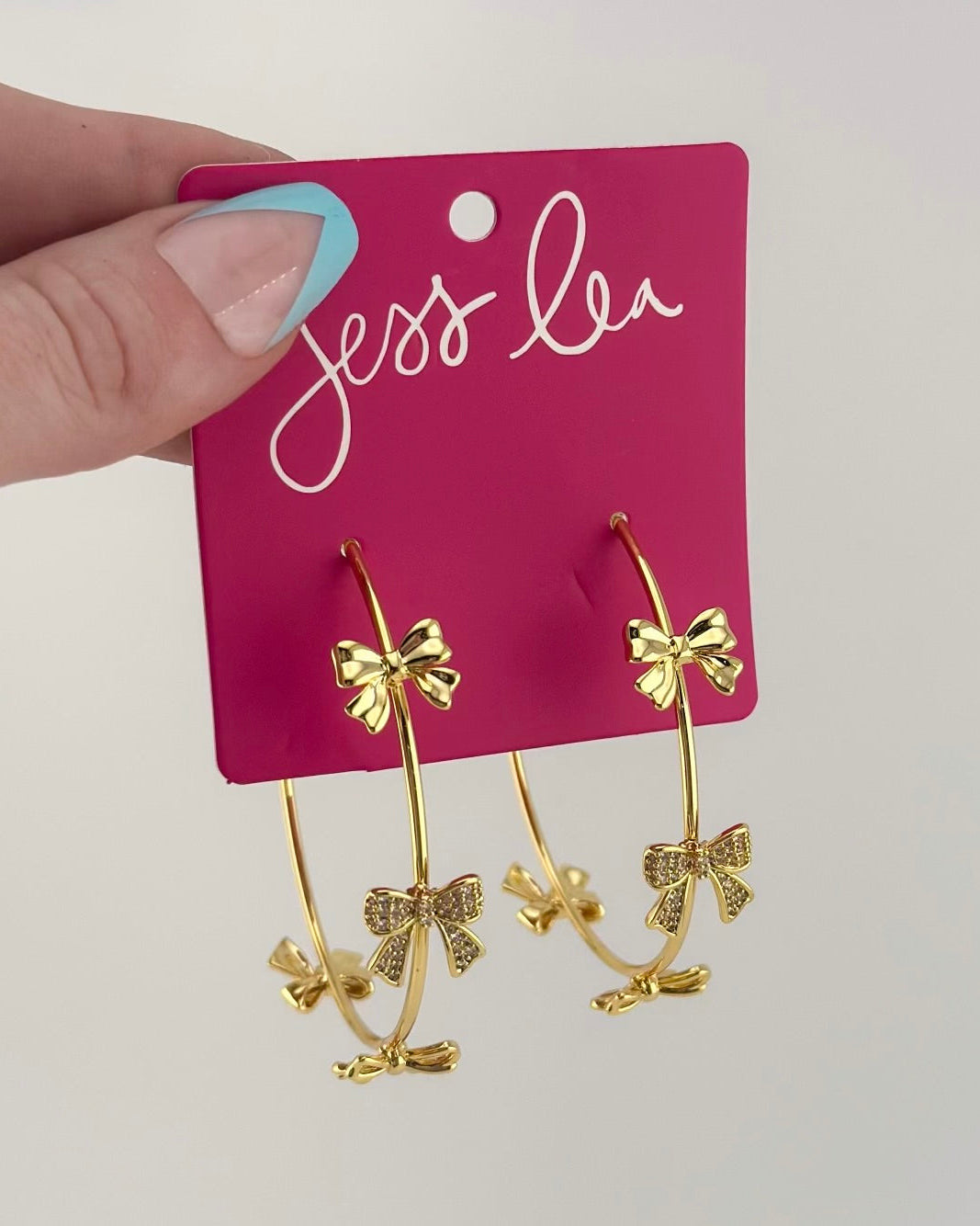gold hoop earring with a post back and a comfort earring back in gold adorned in two solid bows, one open bow, and one bow adorned in rhinestones