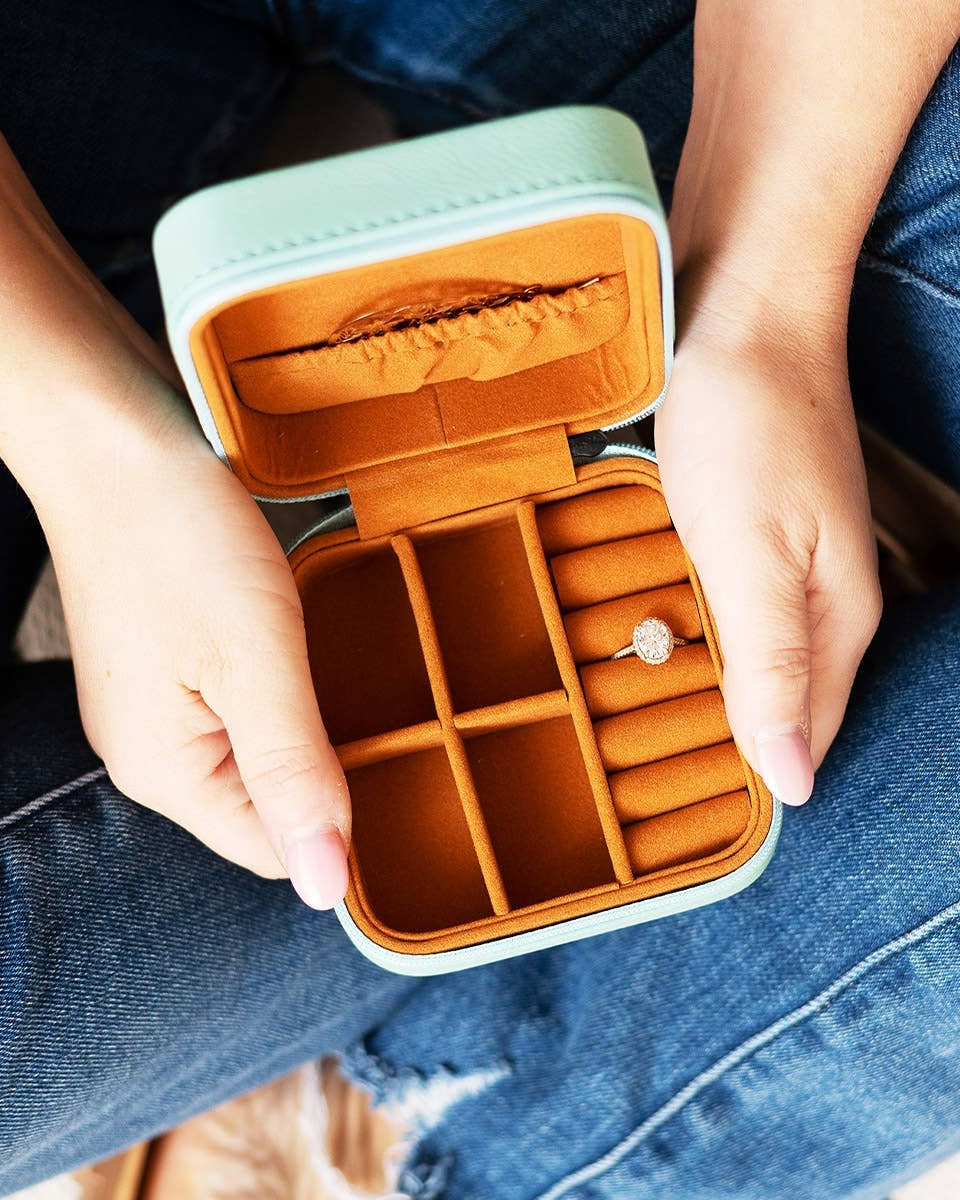 Person holding an open jewelry case with a ring inside, wearing blue jeans.