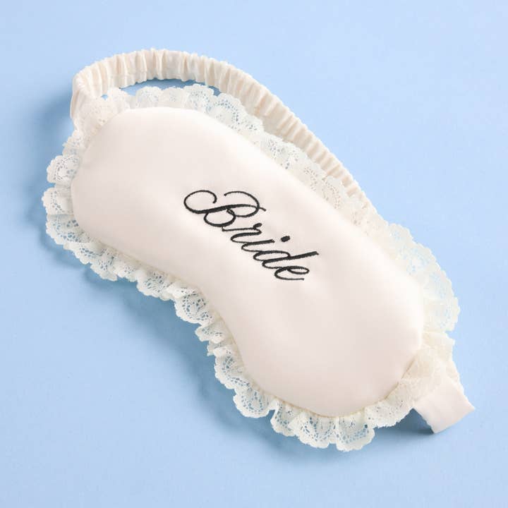 Sleep mask with lace trim and 'Bride' embroidery on a light blue background