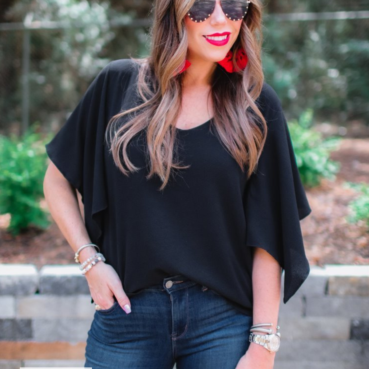 a black v-neck blouses crafted from lightweight textured fabric with asymmetrical half-flutter sleeves, front lining, and a relaxed fit, accented by a MADE IN USA watermark in the bottom left-hand corner