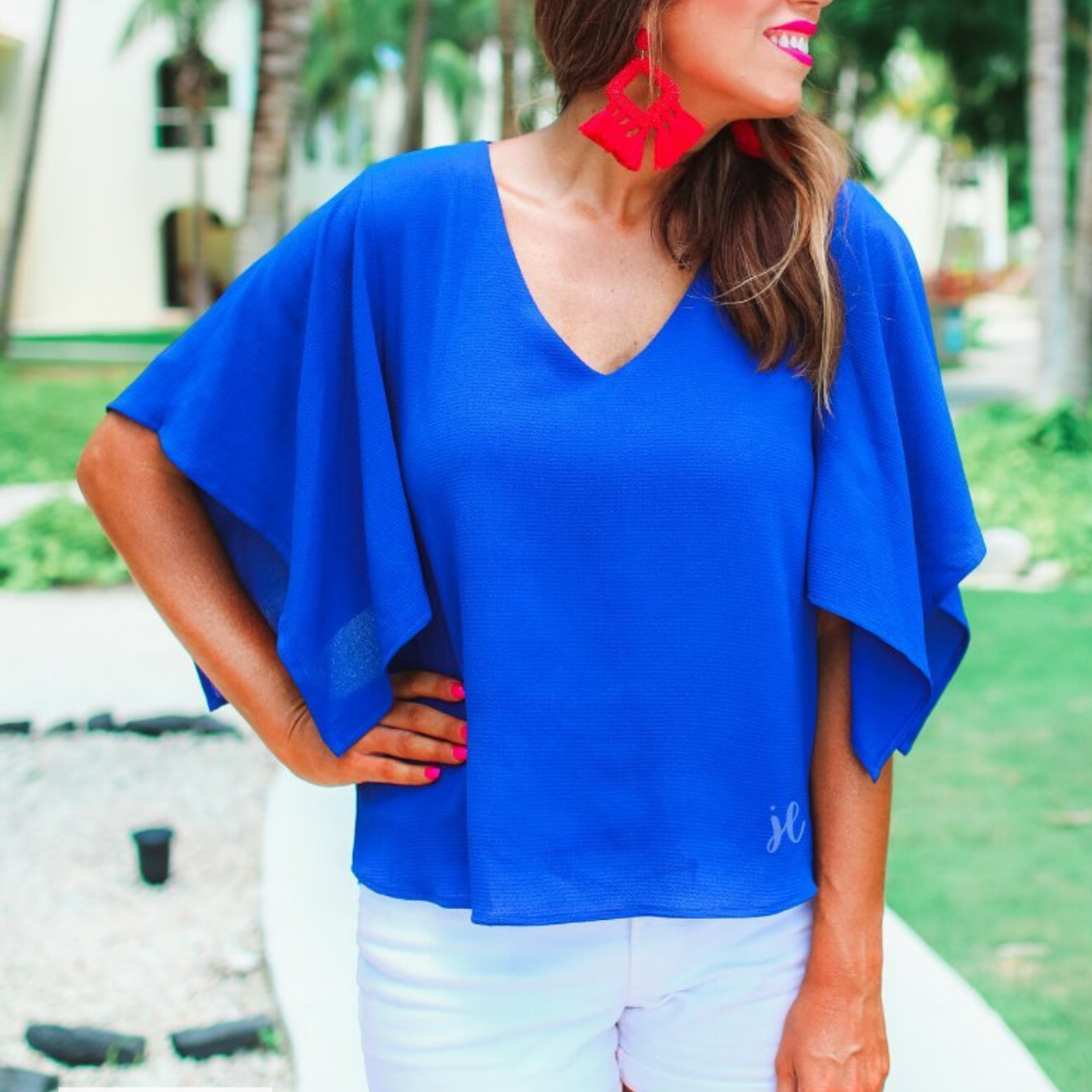 a blue v-neck blouses crafted from lightweight textured fabric with asymmetrical half-flutter sleeves, front lining, and a relaxed fit, accented by a MADE IN USA watermark in the bottom left-hand corner