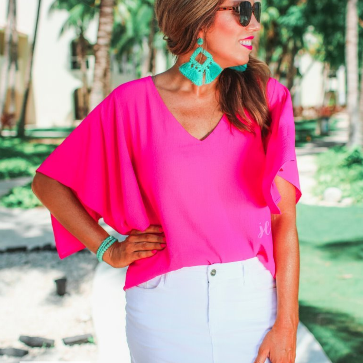 a pink v-neck blouses crafted from lightweight textured fabric with asymmetrical half-flutter sleeves, front lining, and a relaxed fit, accented by a MADE IN USA watermark in the bottom left-hand corner