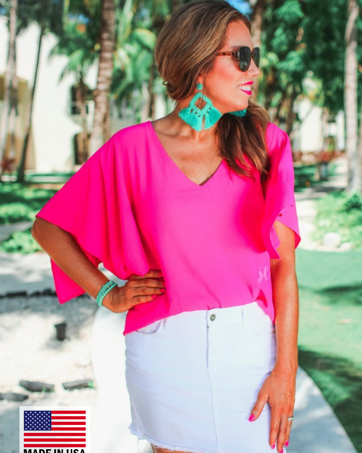a pink v-neck blouses crafted from lightweight textured fabric with asymmetrical half-flutter sleeves, front lining, and a relaxed fit, accented by a MADE IN USA watermark in the bottom left-hand corner