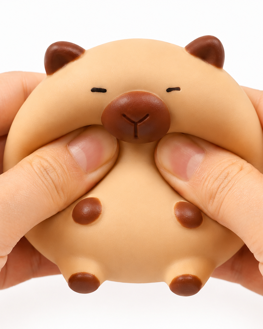 a capybara-inspired squishy toy with a rounded tan body, brown accent details, sleepy face, and smooth squeezable texture being squeezed