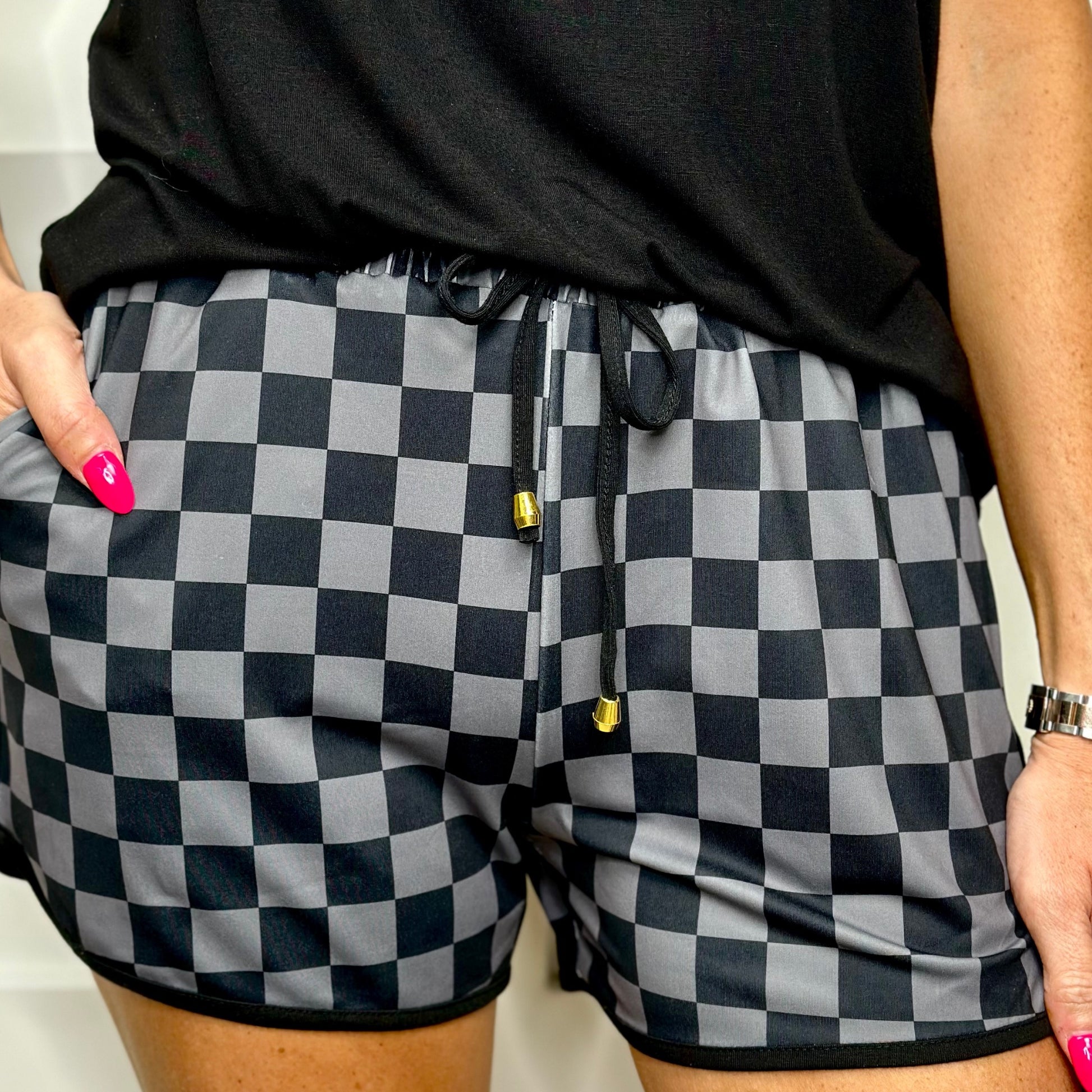 mid-rise relaxed fit activewear shorts with side pockets and a tie waist drawstring with gold bead accents, designed on a two-tone black checkered pattern print fabric and black trim