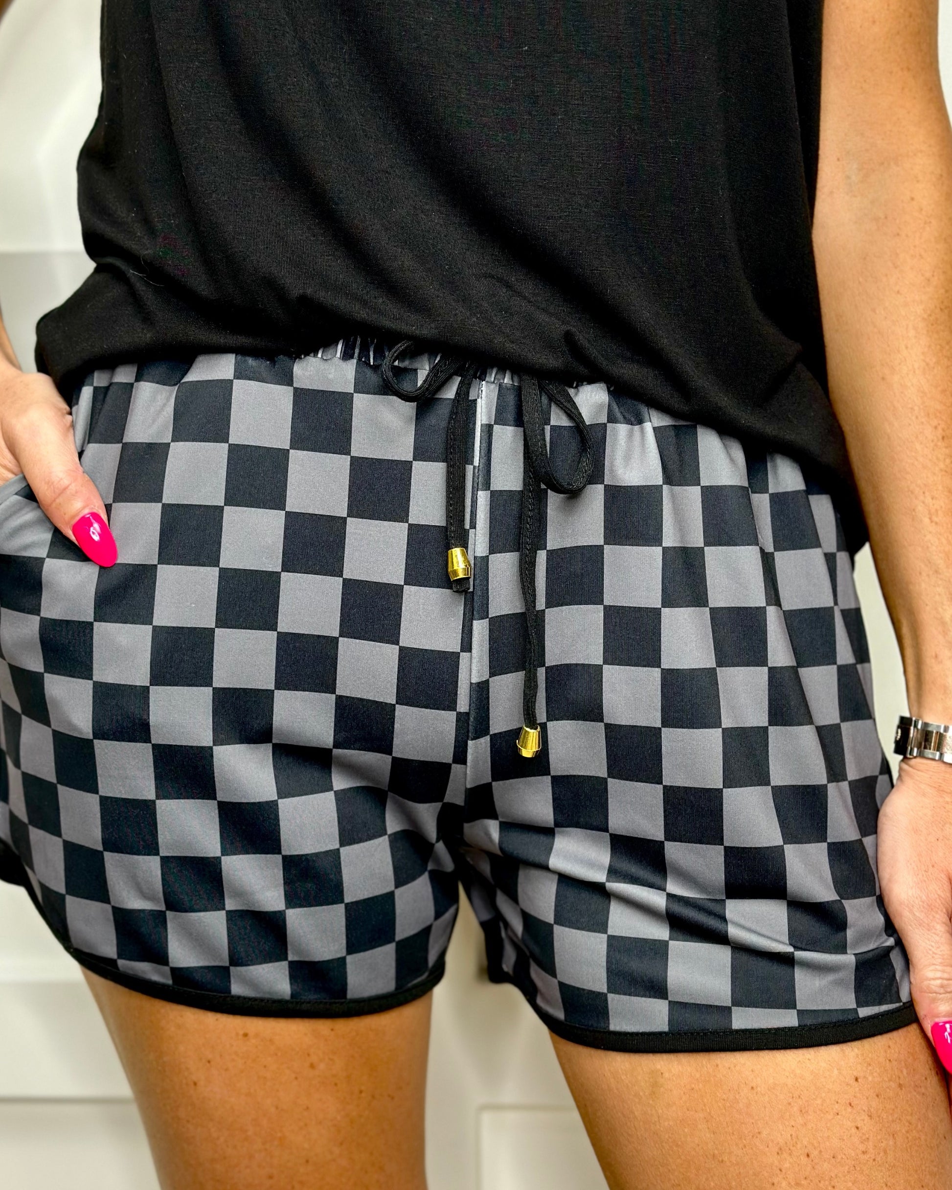 mid-rise relaxed fit activewear shorts with side pockets and a tie waist drawstring with gold bead accents, designed on a two-tone black checkered pattern print fabric and black trim