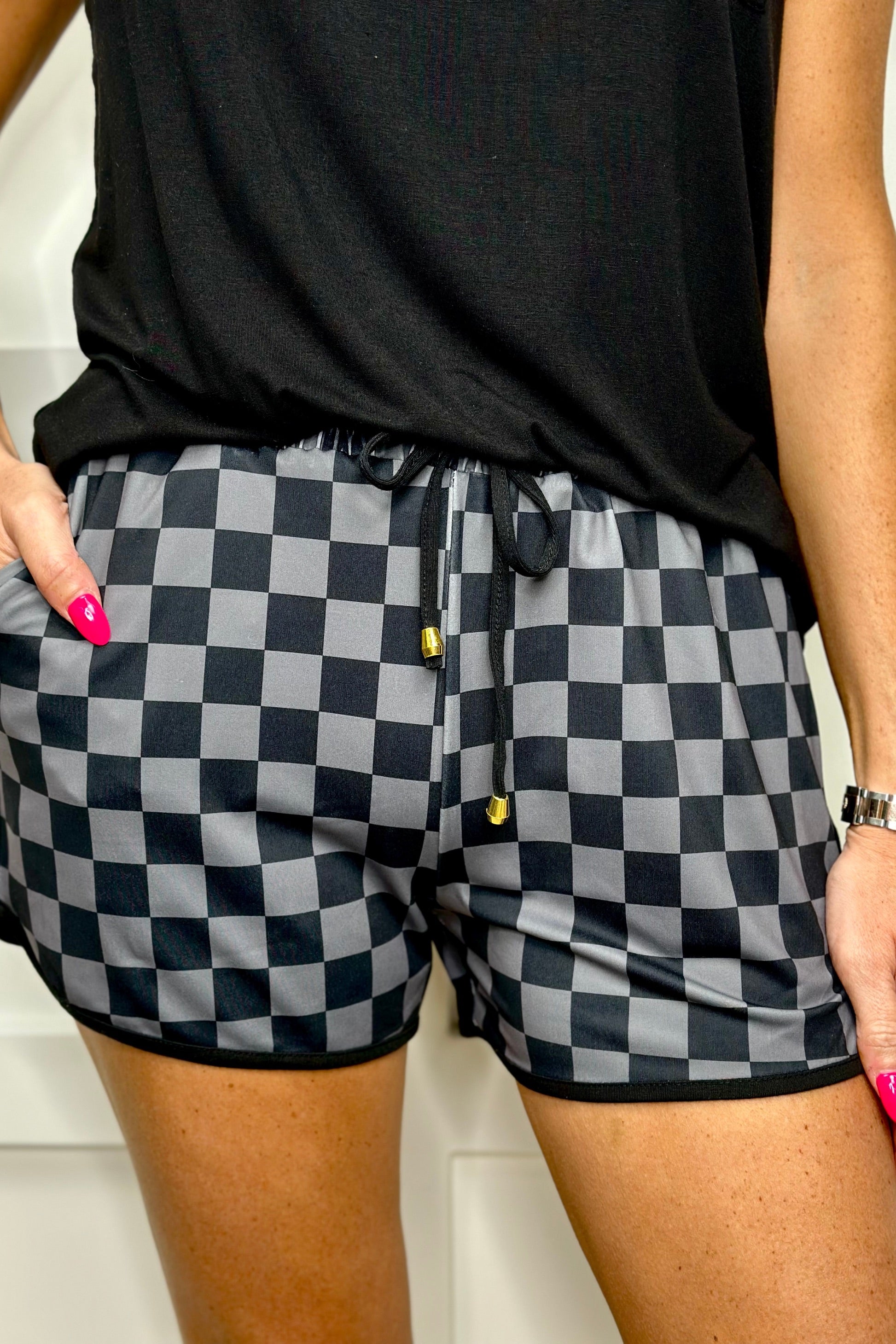 mid-rise relaxed fit activewear shorts with side pockets and a tie waist drawstring with gold bead accents, designed on a two-tone black checkered pattern print fabric and black trim