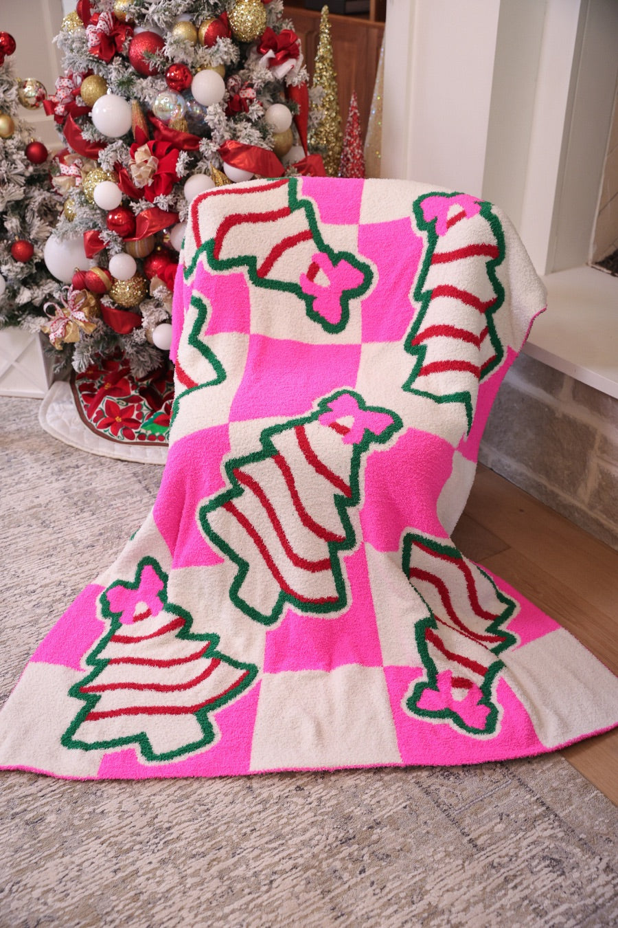 ultra-soft throw on a bold pink and white checkered background decorated with whimsical Christmas tree treats, each topped with an adorable pink bow