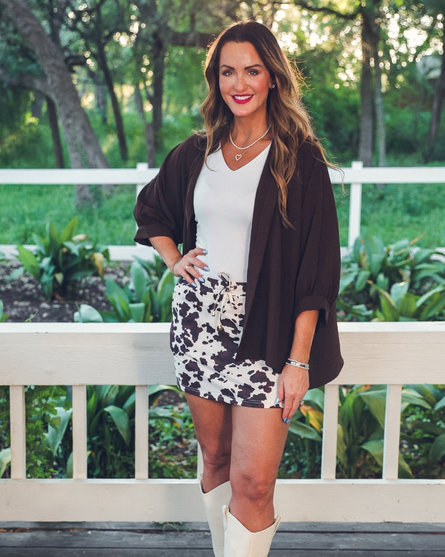 mid-rise relaxed fit everyday skort made of lightweight material with built-in cream shorts, drawstring tie with gold bead accents, an elastic band on the back, and side pockets, designed on a brown cow pattern print fabric and cream base