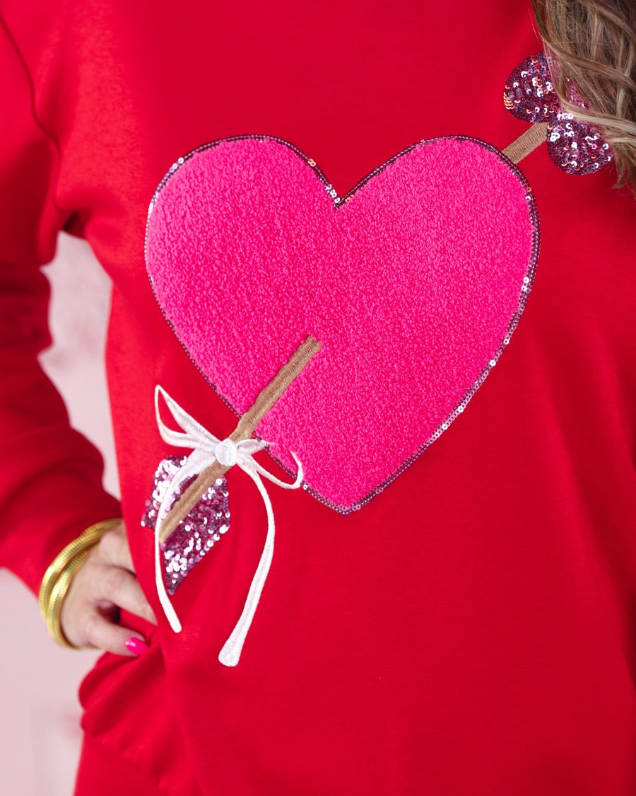 a long-sleeve pullover made from luxe material with a classic crew neckline, a relaxed drop-shoulder fit, and a statement chenille heart accented with intricate embroidery and a sequins bow-and-arrow detail