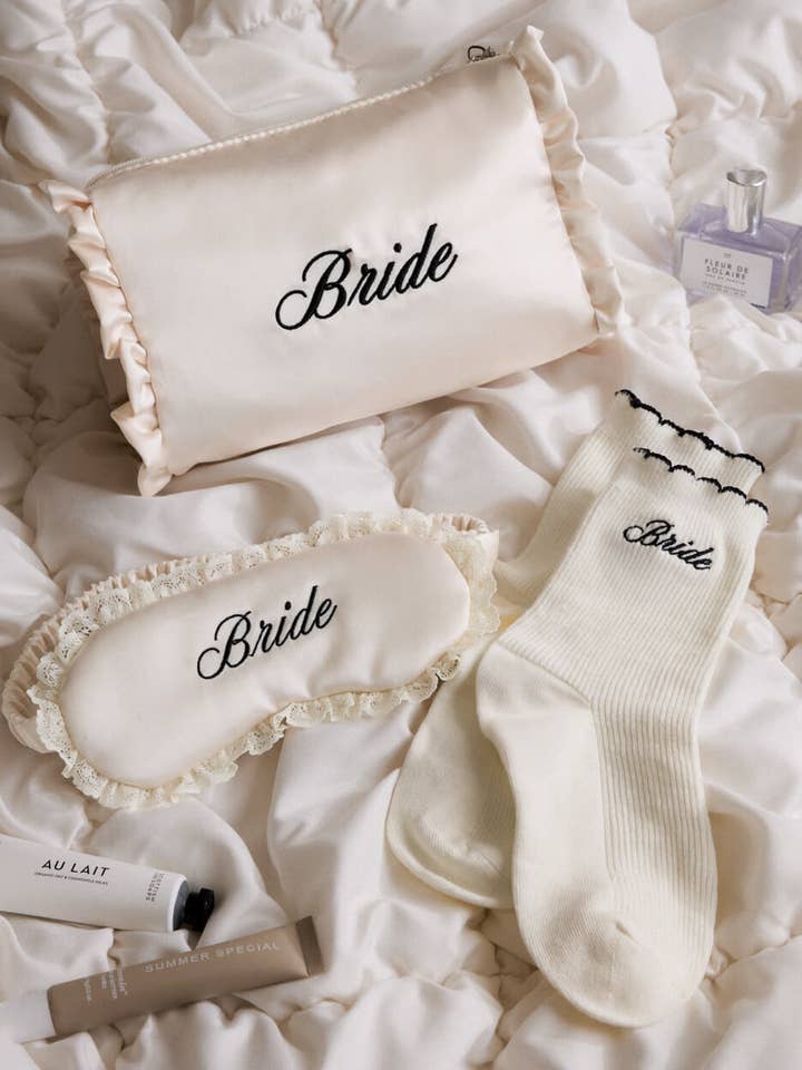 Bride-themed accessories including a pillow, eye mask, and socks on a white surface.