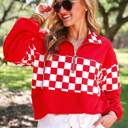 a relaxed red half-zip pullover with gold zipper detail, checkerboard contrast panels, long sleeves, elasticized cuffs, and a softly gathered bottom hem