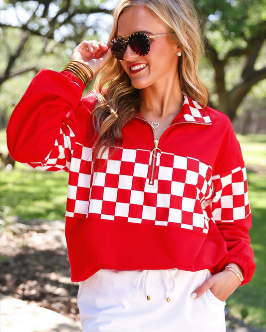 a relaxed red half-zip pullover with gold zipper detail, checkerboard contrast panels, long sleeves, elasticized cuffs, and a softly gathered bottom hem