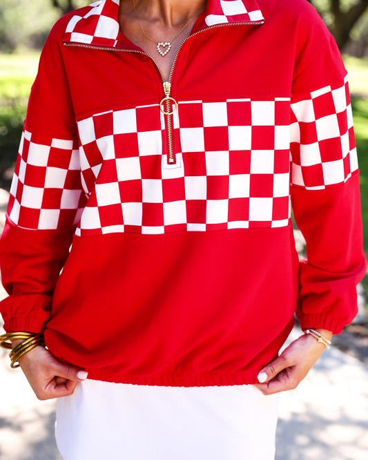 a relaxed red half-zip pullover with gold zipper detail, checkerboard contrast panels, long sleeves, elasticized cuffs, and a softly gathered bottom hem