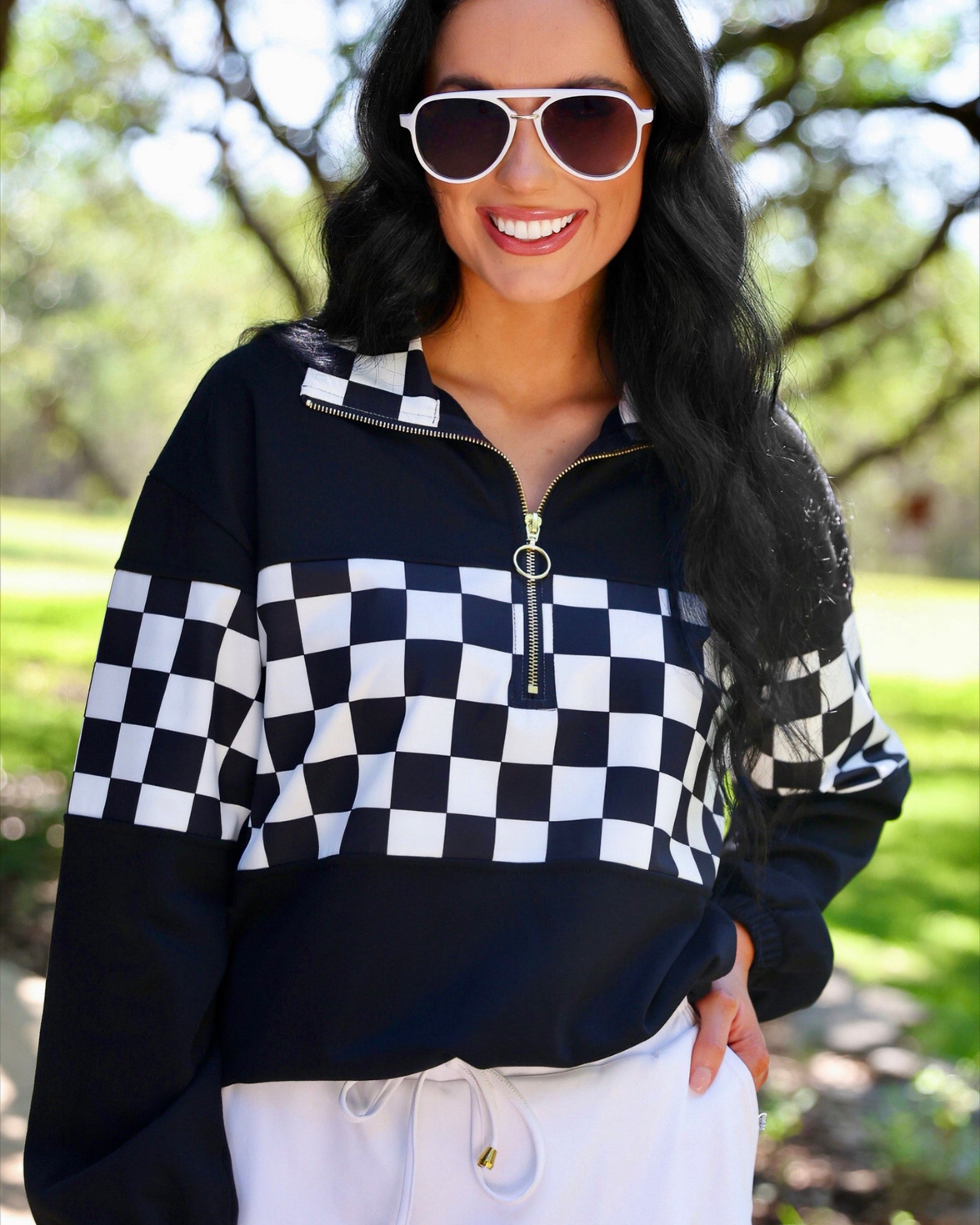 a relaxed black half-zip pullover with gold zipper detail, checkerboard contrast panels, long sleeves, elasticized cuffs, and a softly gathered bottom hem