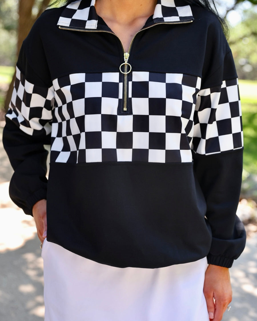 a relaxed black half-zip pullover with gold zipper detail, checkerboard contrast panels, long sleeves, elasticized cuffs, and a softly gathered bottom hem